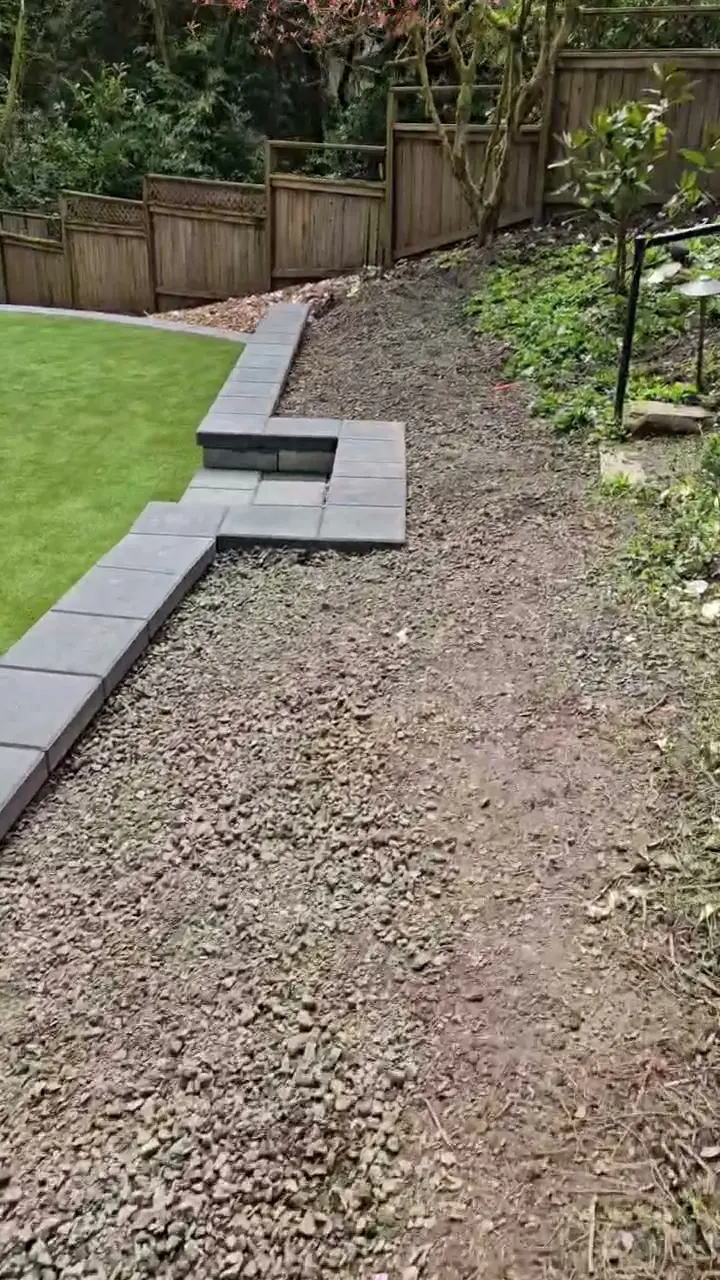 Curved dark block edging beside a Portland backyard lawn and wooded slope